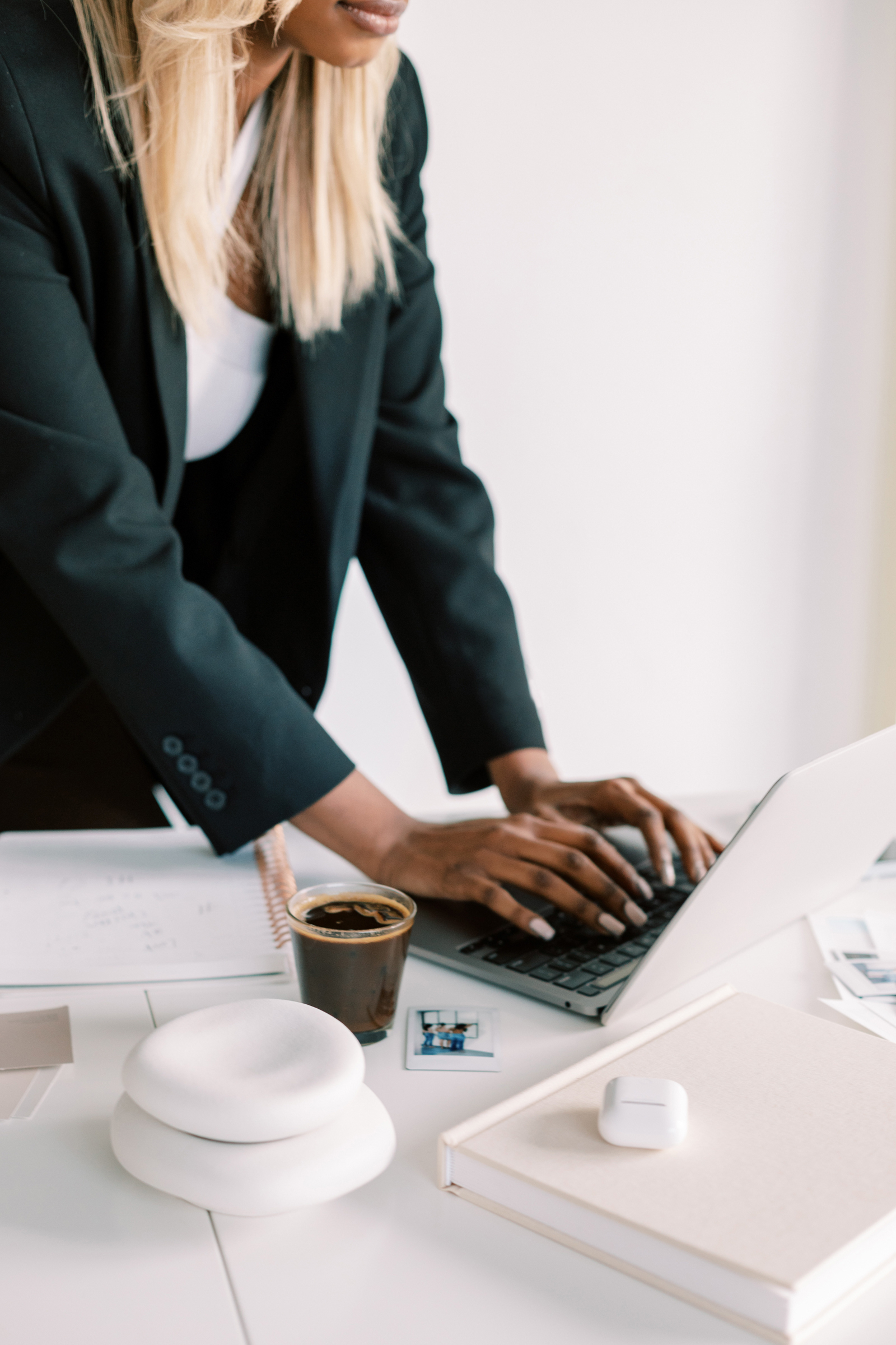 Brown-skinned woman with blonde hair standing at a desk typing on the computer